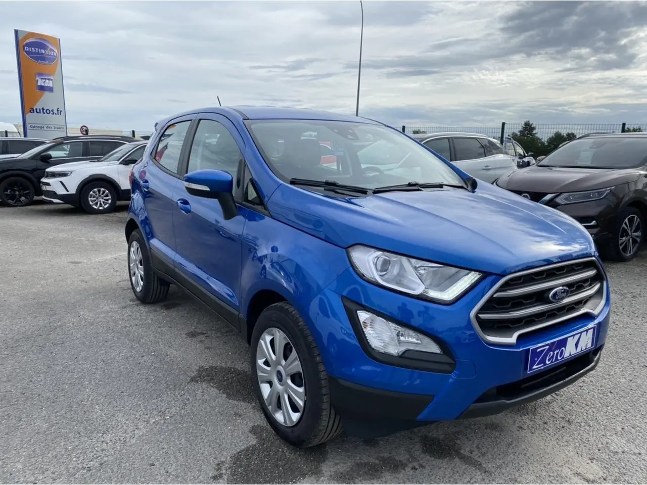 Ford EcoSport bleu Island en 3/4 avant droit, avec projecteurs antibrouillard et calandre chromée visible.