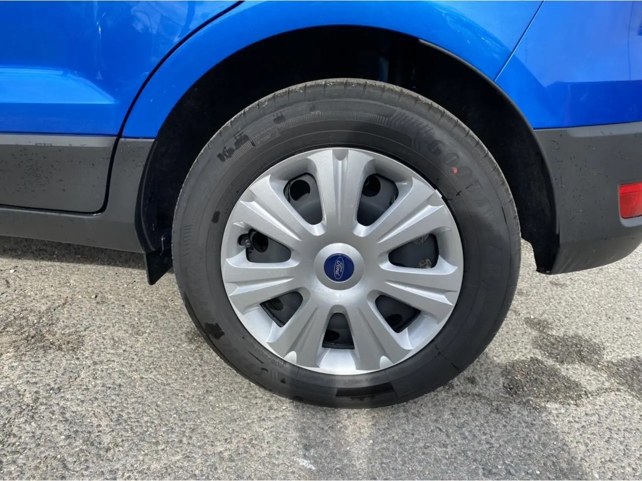 Gros plan sur la roue arrière droite d’un Ford EcoSport bleu Island avec enjoliveur argenté et logo Ford central.