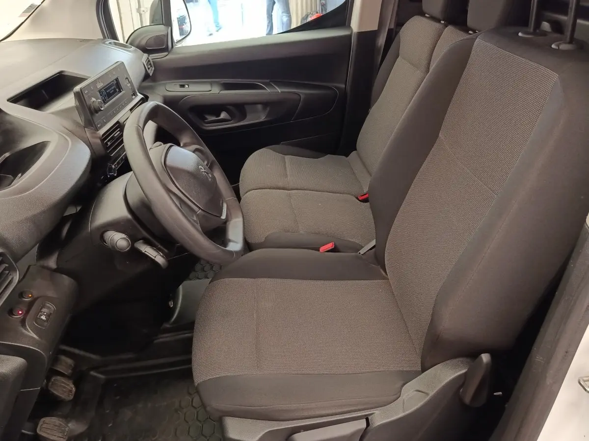 Vue intérieure côté conducteur du Peugeot Partner 2022 blanc, montrant le volant et les sièges avant gris foncé.