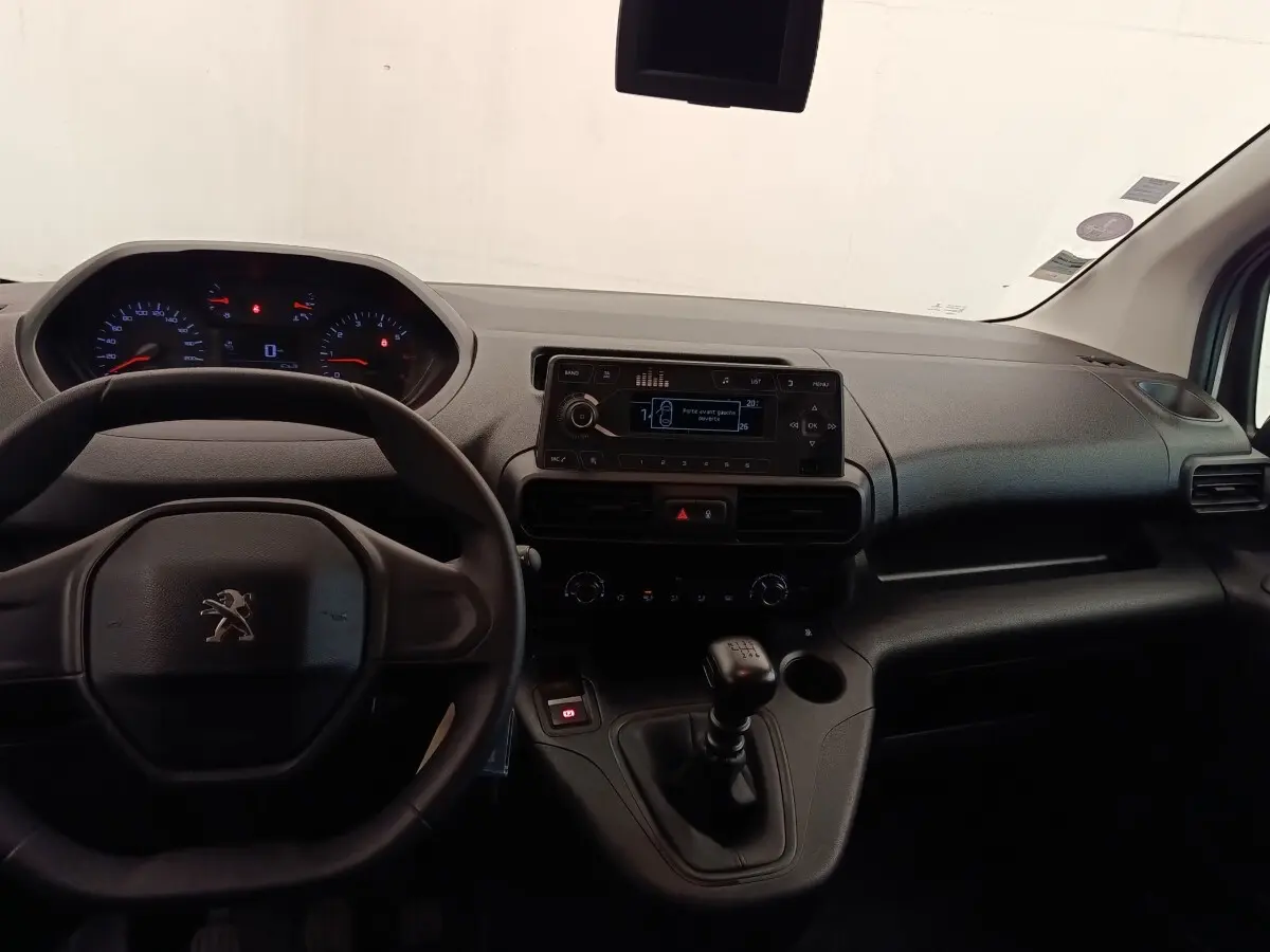 Vue intérieure du tableau de bord du Peugeot Partner blanc 2022, avec volant, écran central et levier de vitesses manuel.