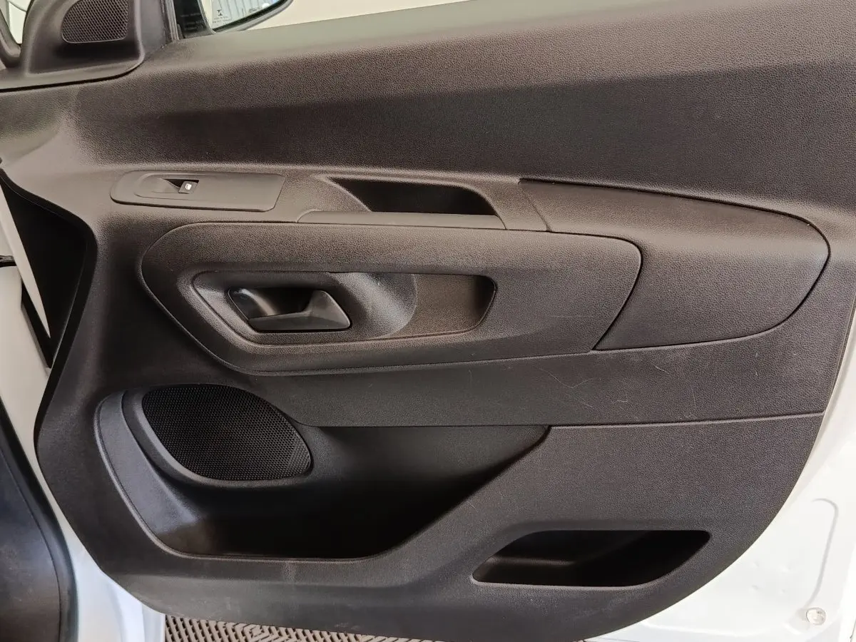 Vue rapprochée de la porte avant gauche noire du Peugeot Partner blanc, avec poignée intérieure et haut-parleur intégré.