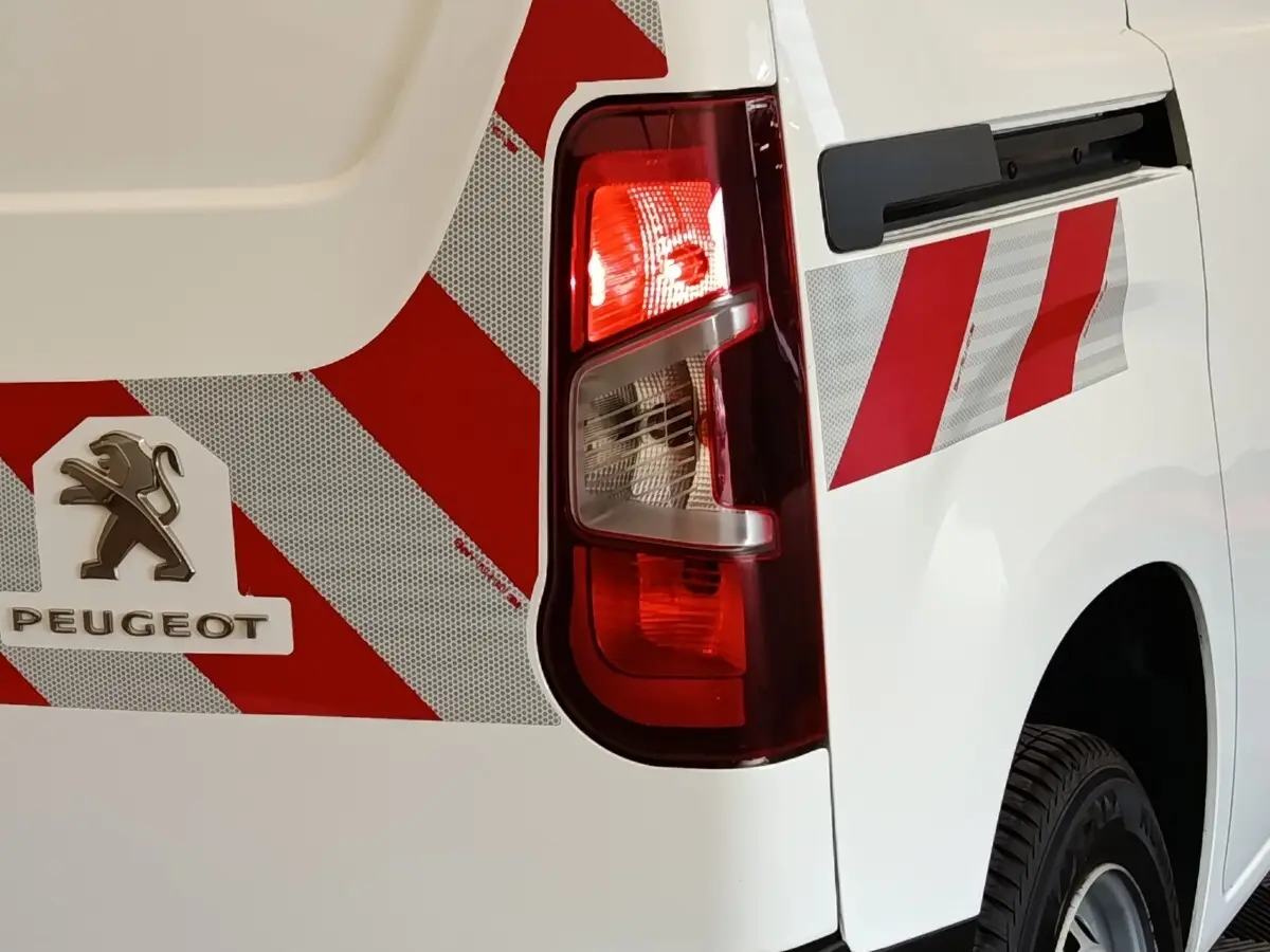Gros plan sur l'arrière droit blanc du Peugeot Partner 2022 avec bandes rouges réfléchissantes et feu arrière allumé.