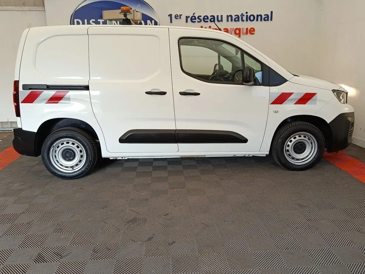 Vue de profil côté droit d’un utilitaire Peugeot Partner blanc avec bandes réfléchissantes rouges et jantes acier.