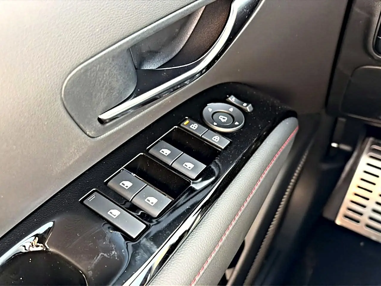 Gros plan sur la commande des vitres côté conducteur du Hyundai Tucson gris shadow, avec surpiqûres rouges et poignée chromée.
