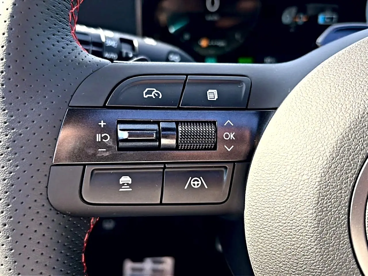 Gros plan sur les commandes noires à gauche du volant cuir perforé avec surpiqûres rouges du Hyundai Tucson gris shadow 2026.