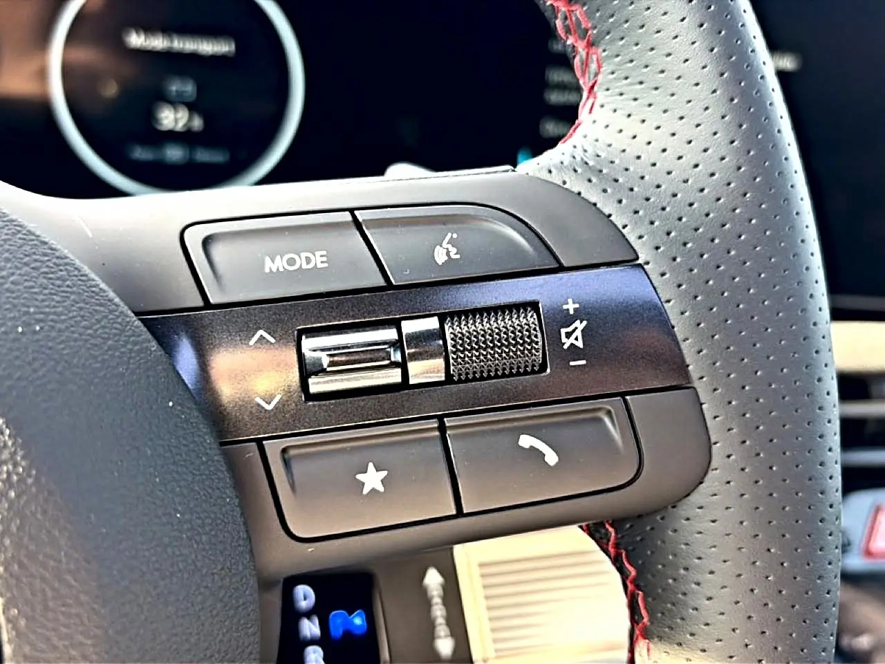 Gros plan sur les commandes gauche du volant cuir perforé gris avec surpiqûres rouges du Hyundai Tucson 2026.