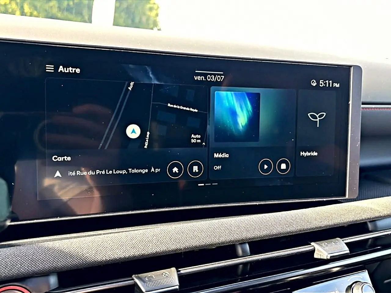 Écran tactile central du Hyundai Tucson 2026 affichant navigation, média et mode hybride, avec tableau de bord gris et détails rouges.