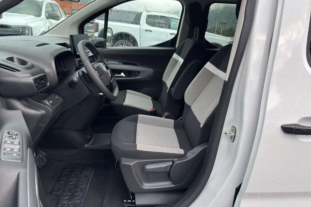 Vue intérieure côté conducteur du Citroën Berlingo Kaolin white 2026, sièges tissu bicolores et volant multifonctions cuir.