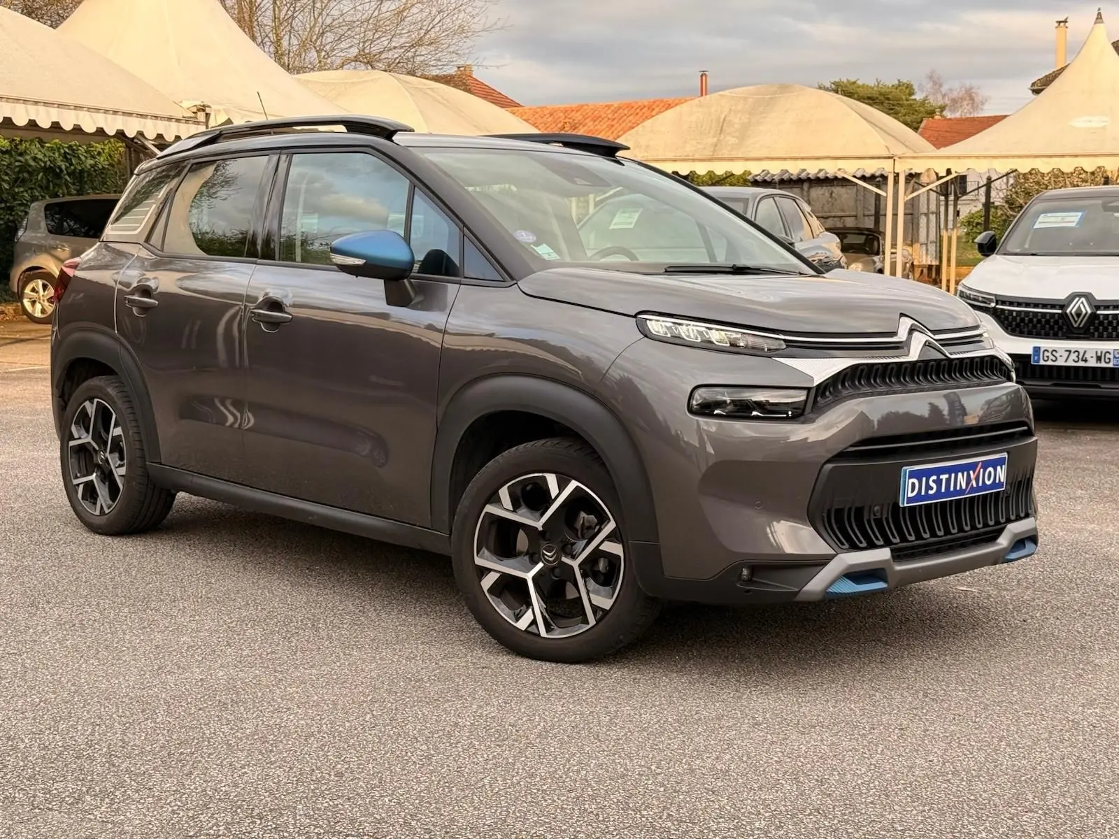 Vue 3/4 avant droit d'un Citroën C3 Aircross gris platinium avec jantes noires et détails bleus sur le bouclier avant.