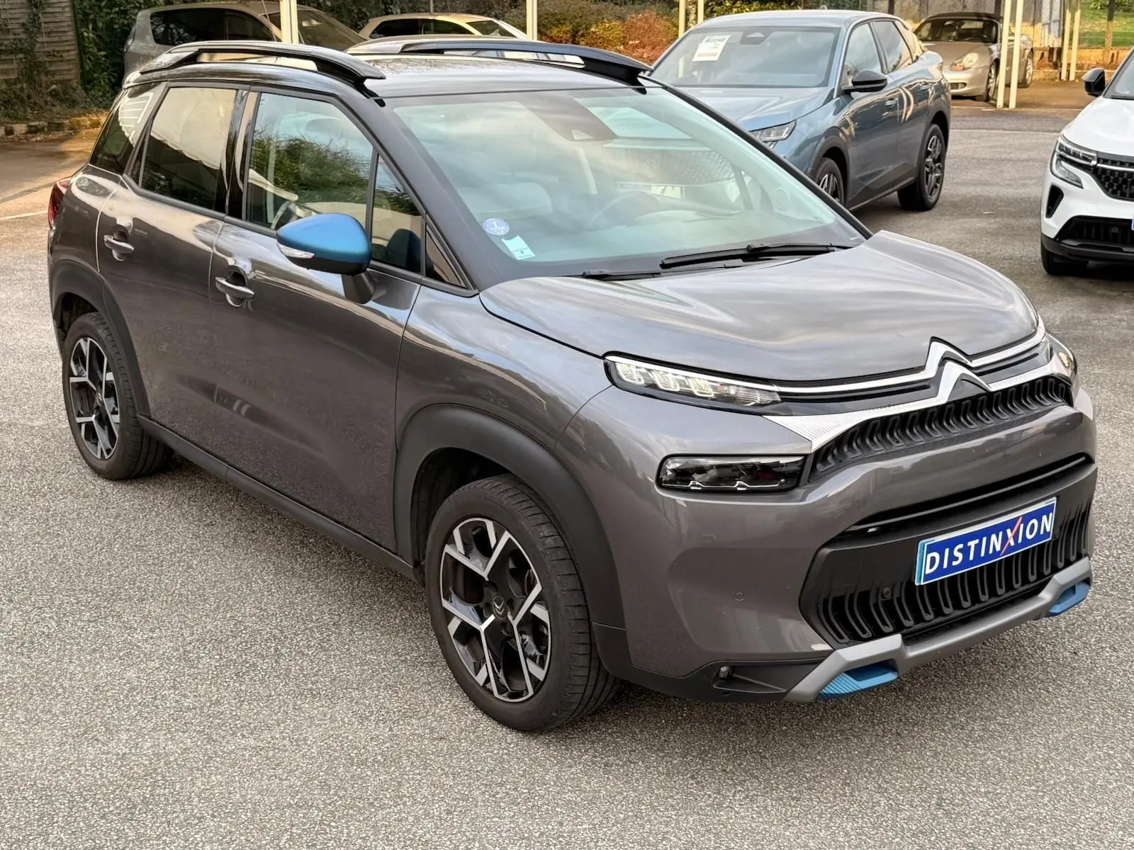 Citroën C3 Aircross gris platinium vue 3/4 avant droit avec rétroviseur bleu et détails bleus sur le pare-chocs.