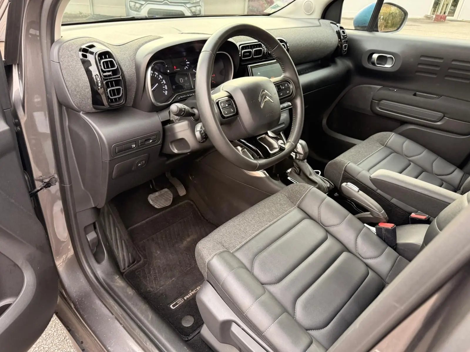 Vue intérieure côté conducteur du Citroën C3 Aircross gris platinium, montrant le tableau de bord et les sièges en cuir et tissu.