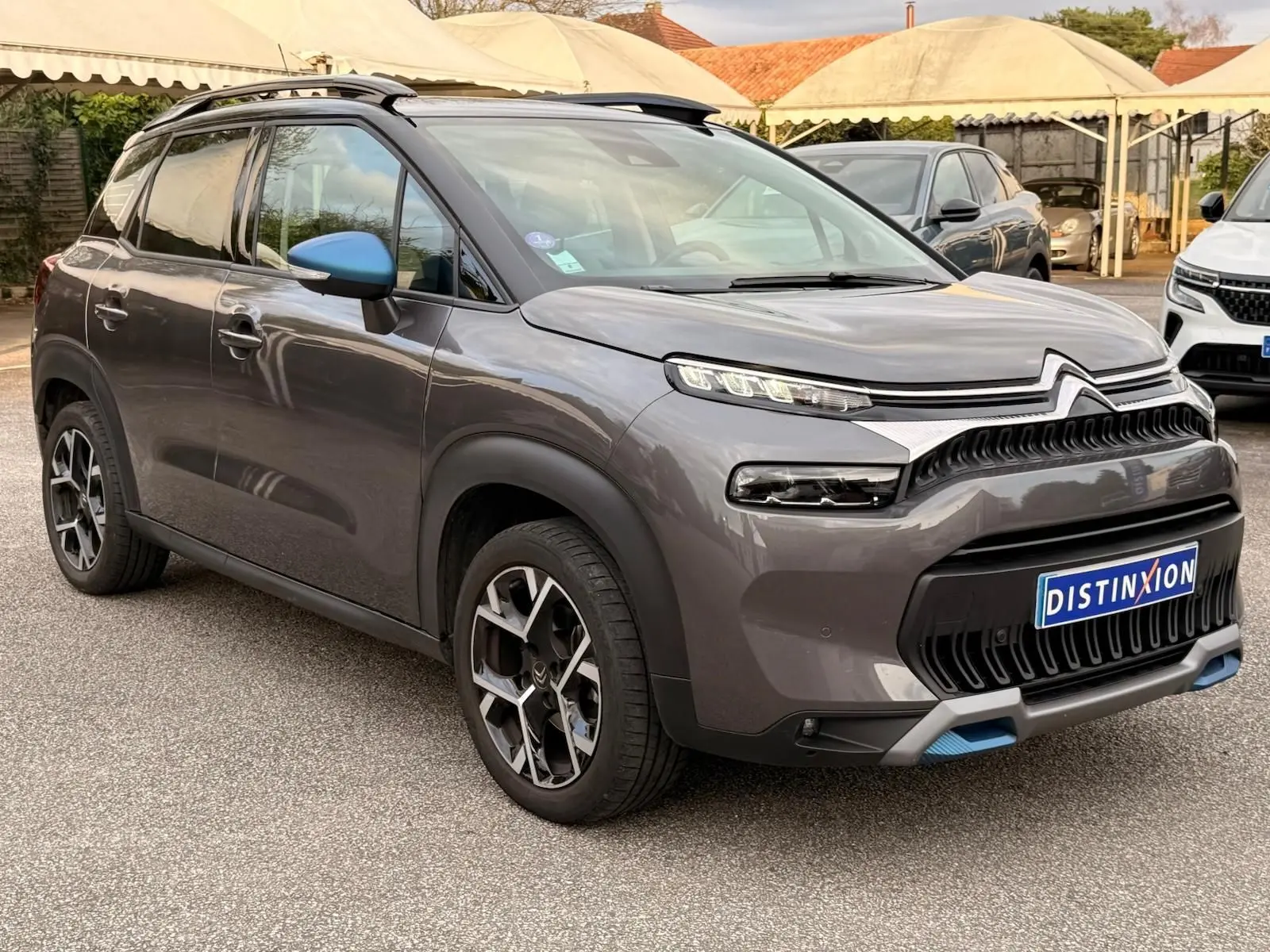Vue 3/4 avant droite d'un Citroën C3 Aircross gris platinium avec détails bleus sur le bouclier et les rétroviseurs.