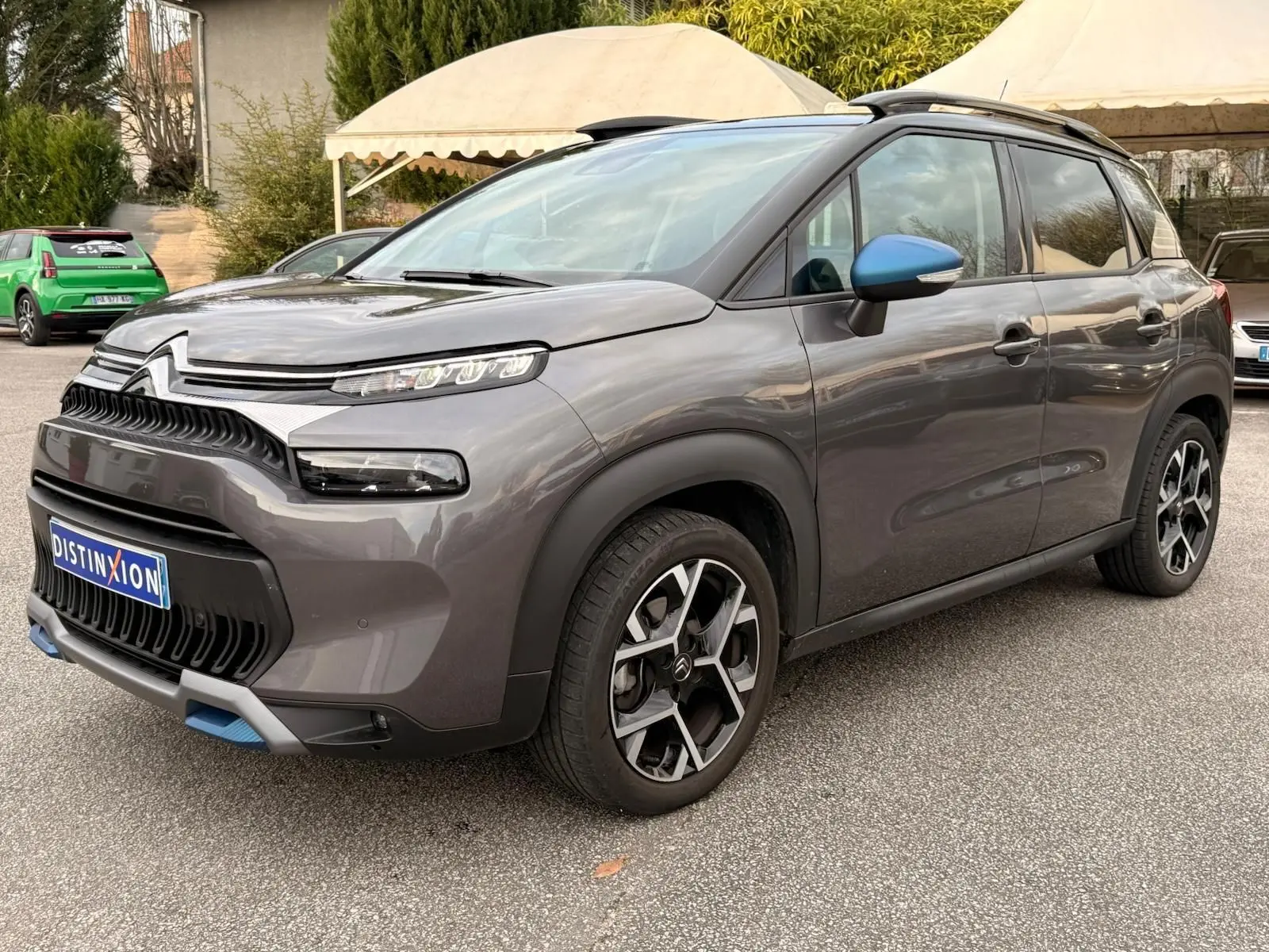 Vue 3/4 avant droit d'un Citroën C3 Aircross gris platinium avec rétroviseurs bleus et jantes noires à motifs géométriques.