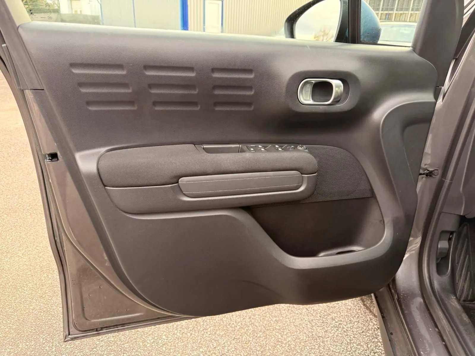 Vue intérieure de la porte avant gauche d'une Citroën C3 Aircross gris platinium avec commandes de vitres et poignée intégrée.