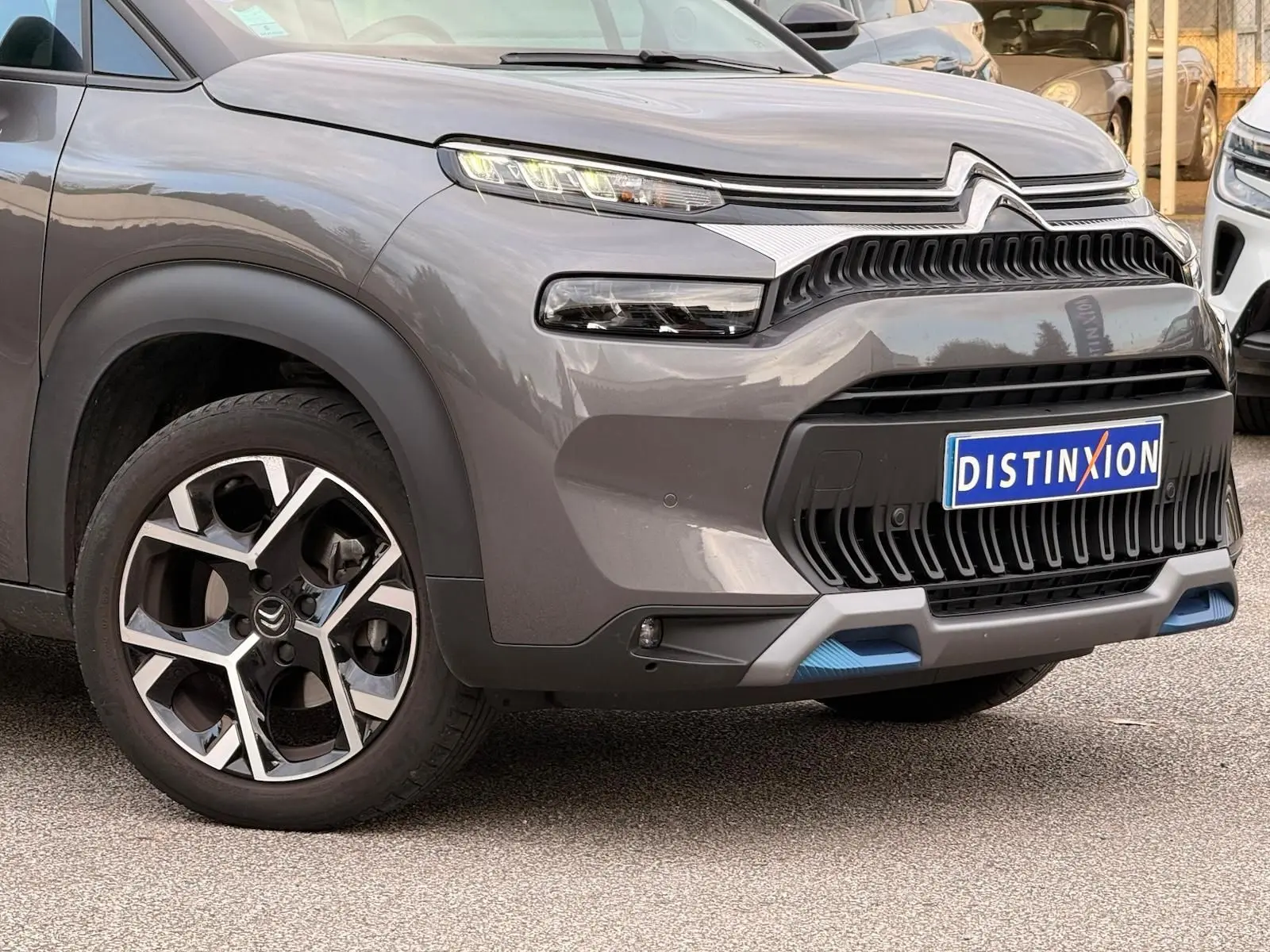 Vue 3/4 avant gauche d'un Citroën C3 Aircross gris platinium avec calandre noire et détails bleus sur le pare-chocs.