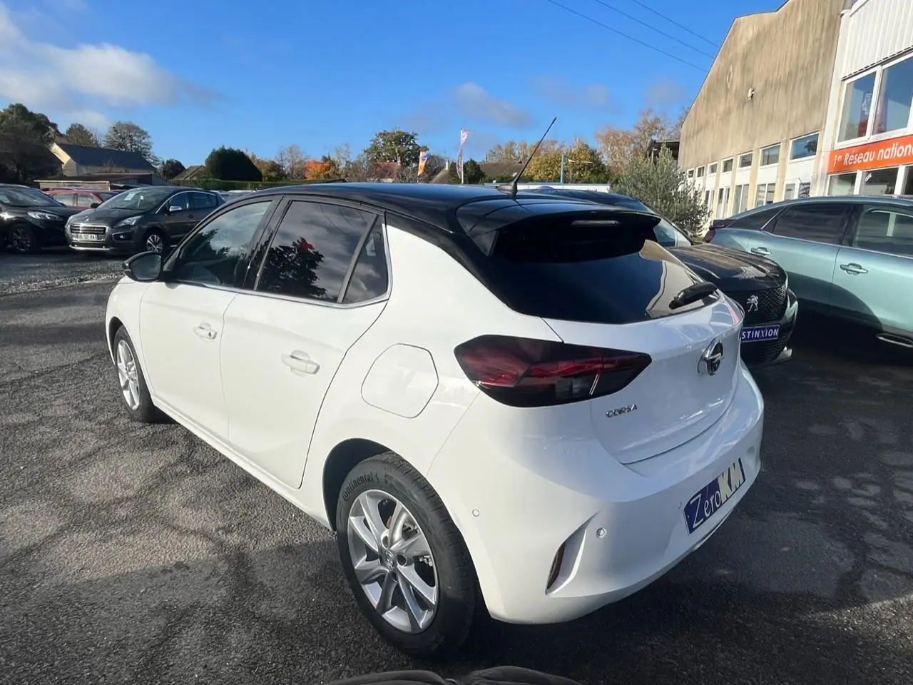 Opel Corsa blanche vue 3/4 arrière droit, toit noir, vitres arrière surteintées et rétroviseurs noirs.