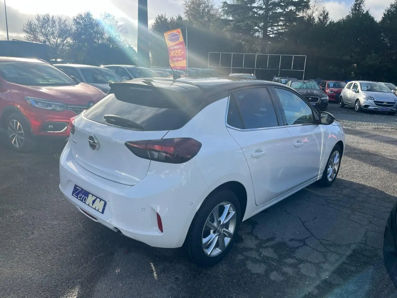 Opel Corsa blanche vue 3/4 arrière droit avec toit noir et feux arrière fumés sur parking extérieur.
