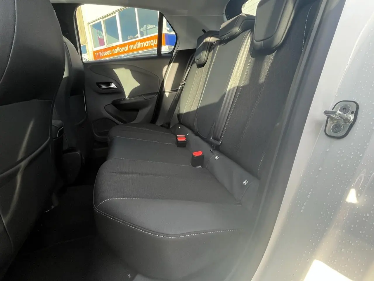 Vue intérieure de la banquette arrière noire de l’Opel Corsa blanche, porte arrière droite ouverte.