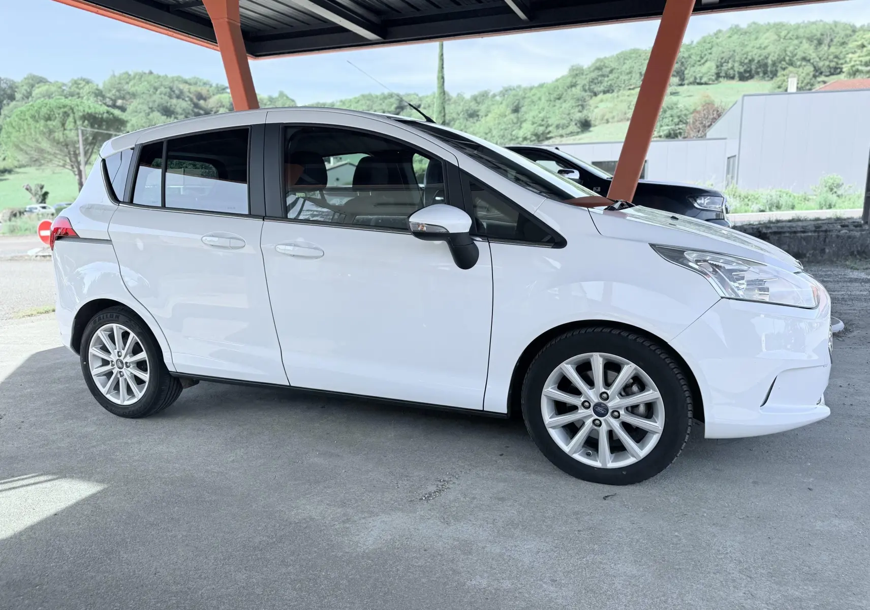 Vue de profil côté droit d'une Ford B-MAX blanche 2017 stationnée sous abri avec jantes alliage visibles.