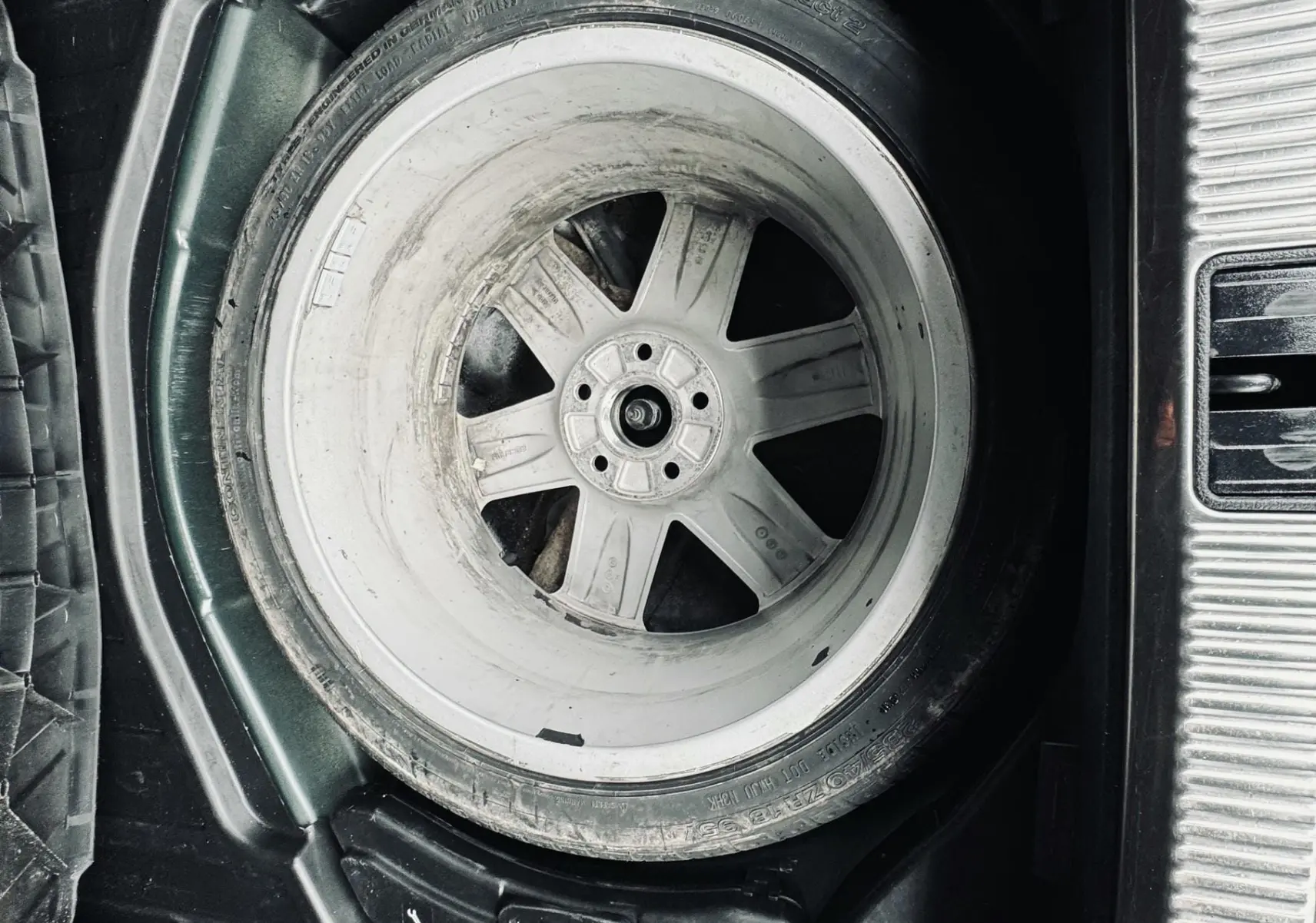 Gros plan sur la roue de secours dans le coffre d'une Audi S4 Avant verte, montrant la jante en aluminium.