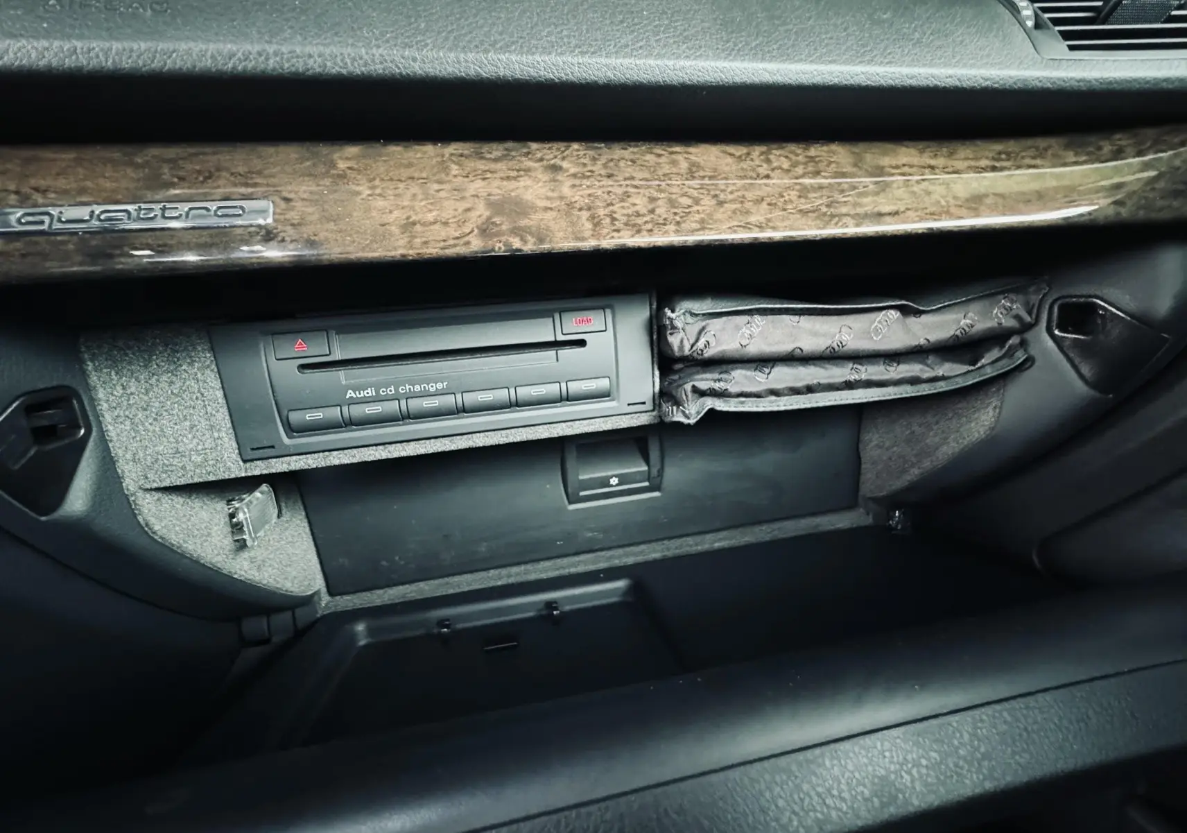 Gros plan sur la boîte à gants ouverte de l'Audi S4 Avant 2004 avec lecteur CD et finition bois brun.