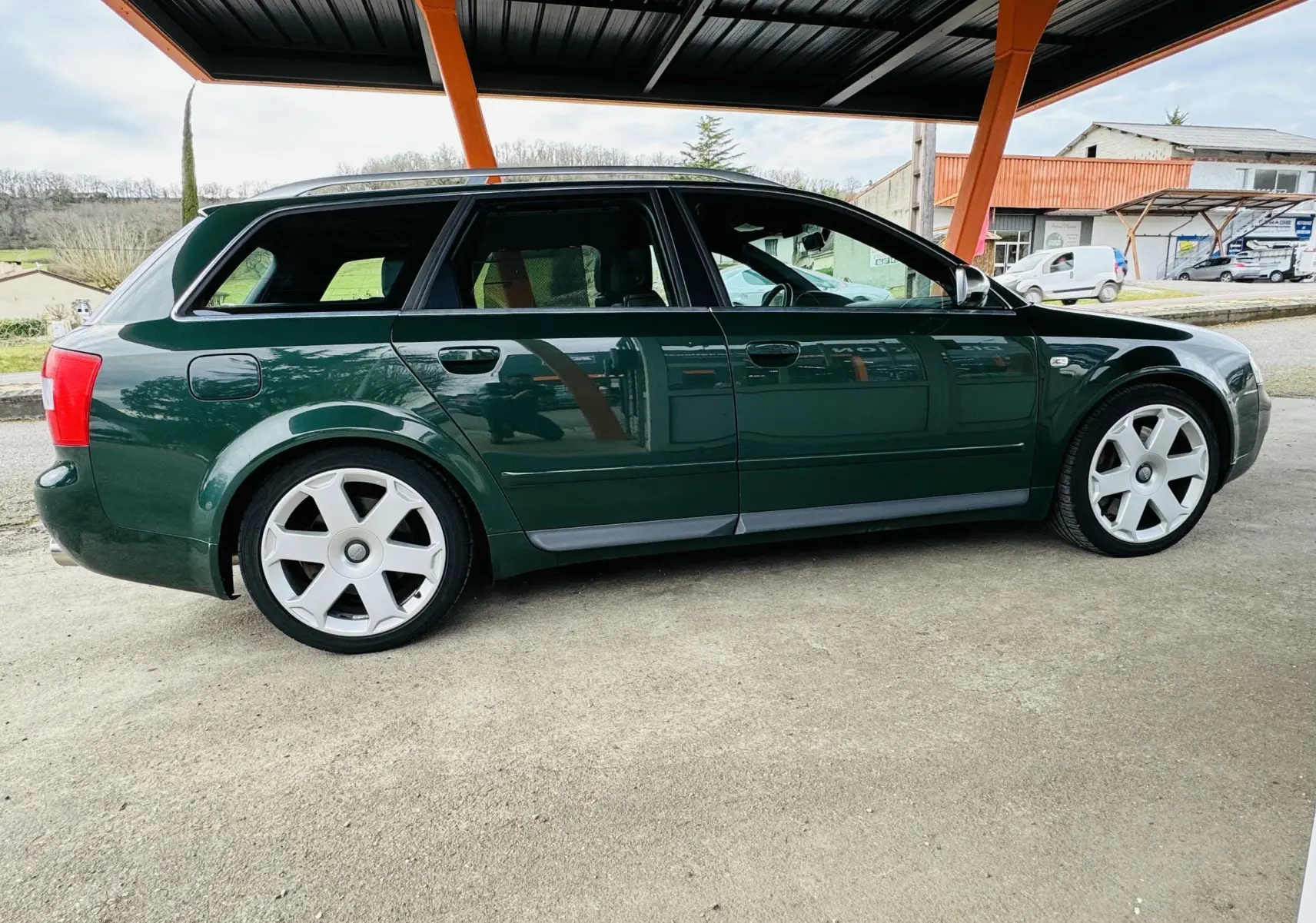 Profil côté gauche d'une Audi S4 Avant 2004 vert foncé avec jantes alliage et toit partiellement couvert.