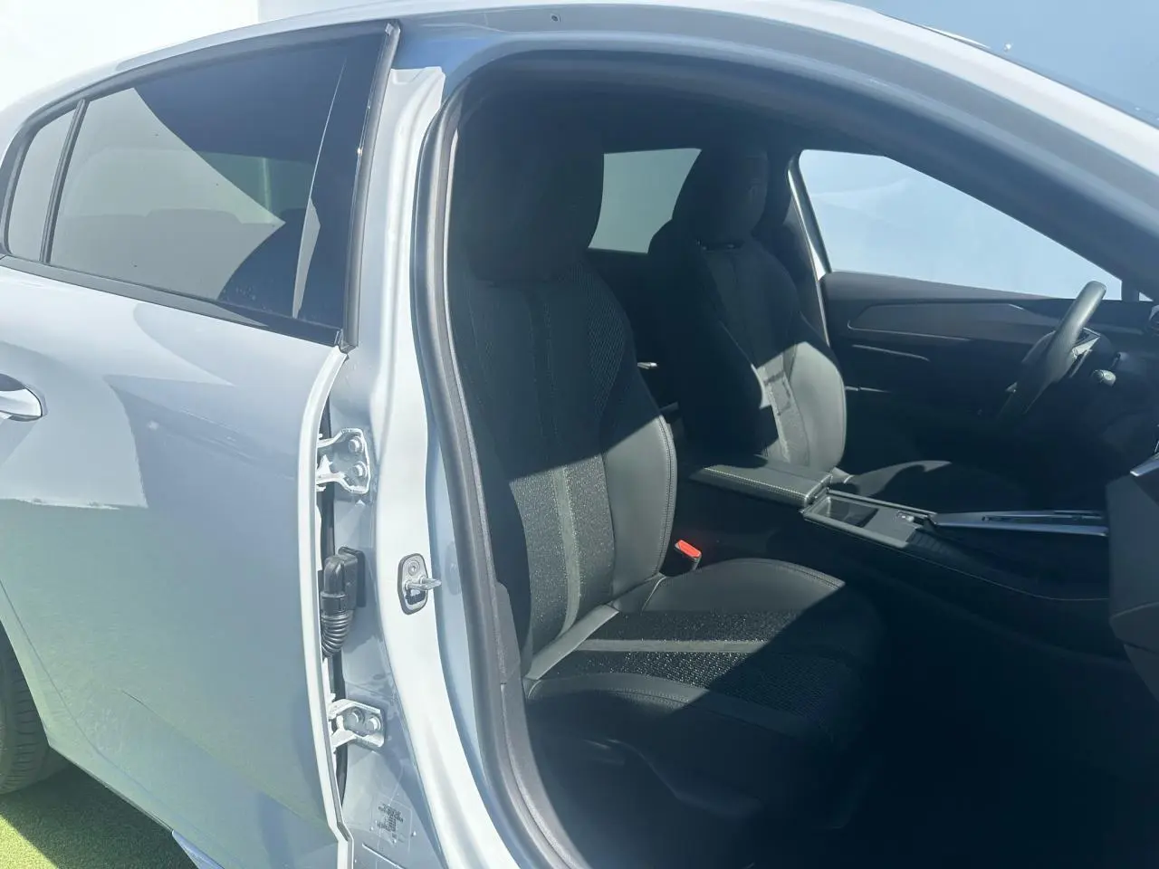 Vue côté gauche intérieur d'une Peugeot 308 blanche Okenite, sièges avant en tissu et cuir noir avec console centrale visible.