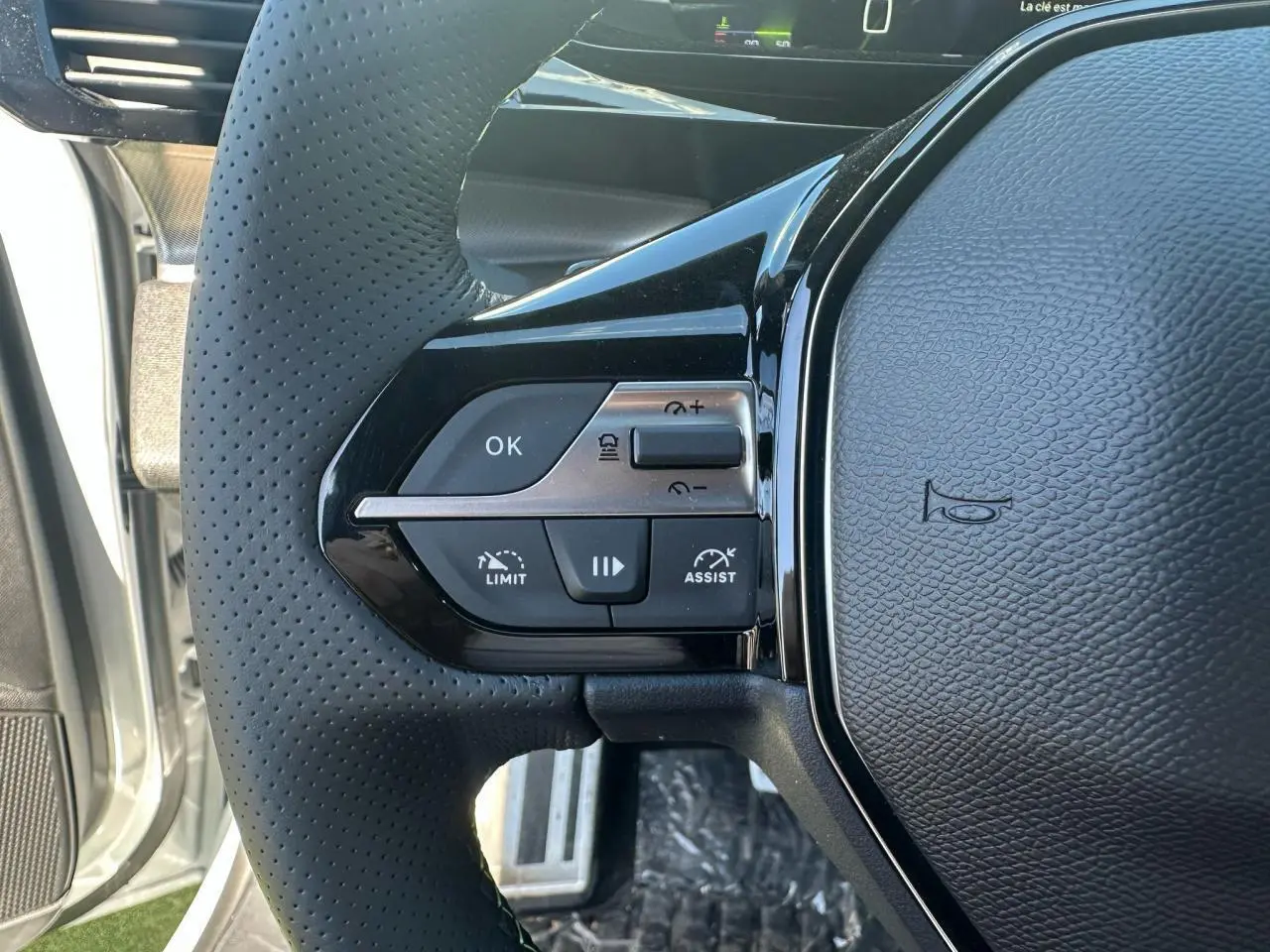 Gros plan sur le côté gauche du volant cuir perforé de la Peugeot 308 blanche avec commandes d'assistance et limitation de vitesse.