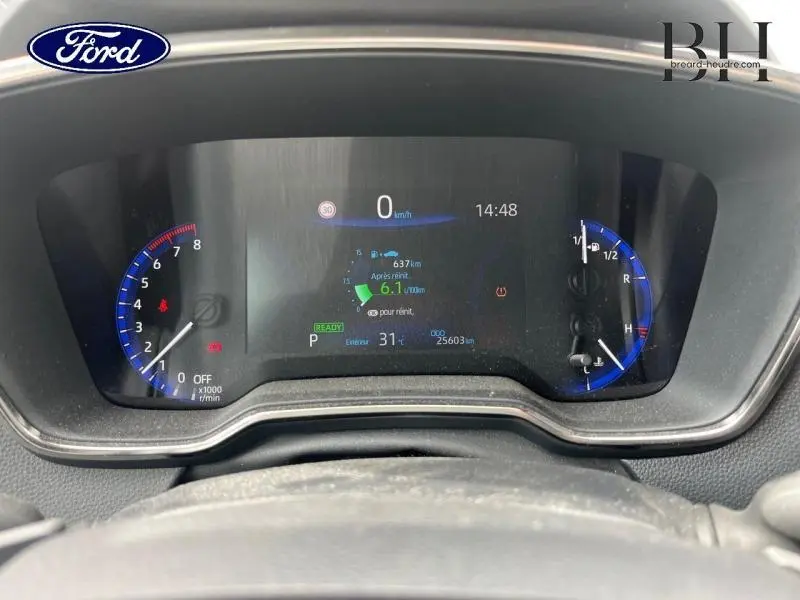 Vue rapprochée du tableau de bord numérique d'une Toyota Corolla blanche, affichant les compteurs et informations de conduite.