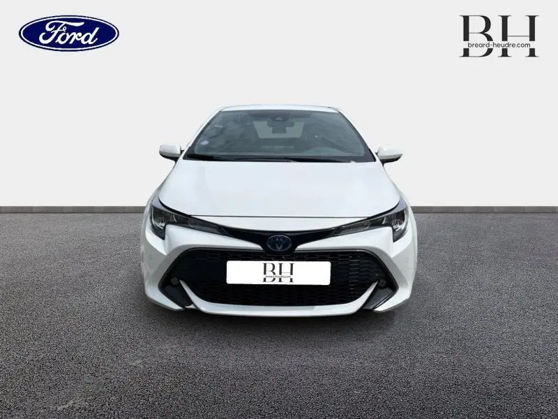 Vue de face d'une Toyota Corolla blanche Pure avec calandre noire et phares LED fins, sur fond neutre.