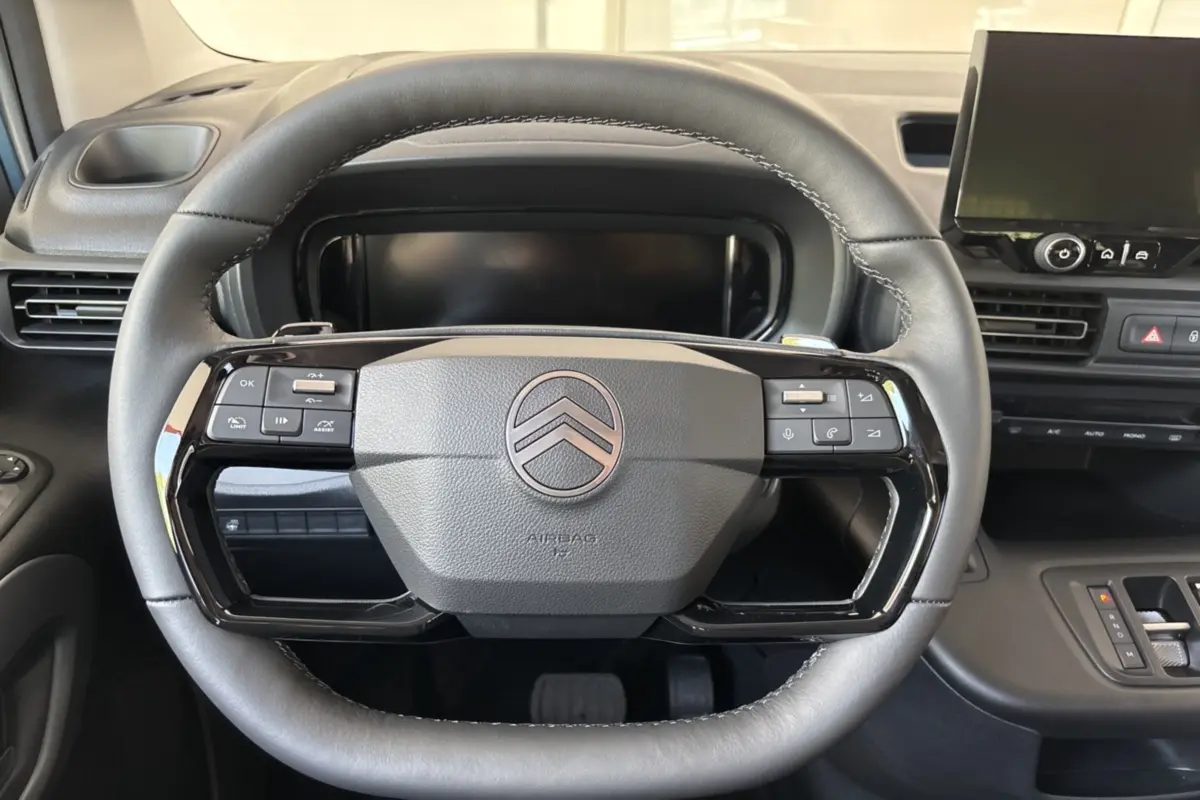 Vue rapprochée du volant cuir multifonctions noir du Citroën Berlingo 2026 avec tableau de bord et écran tactile en arrière-plan.