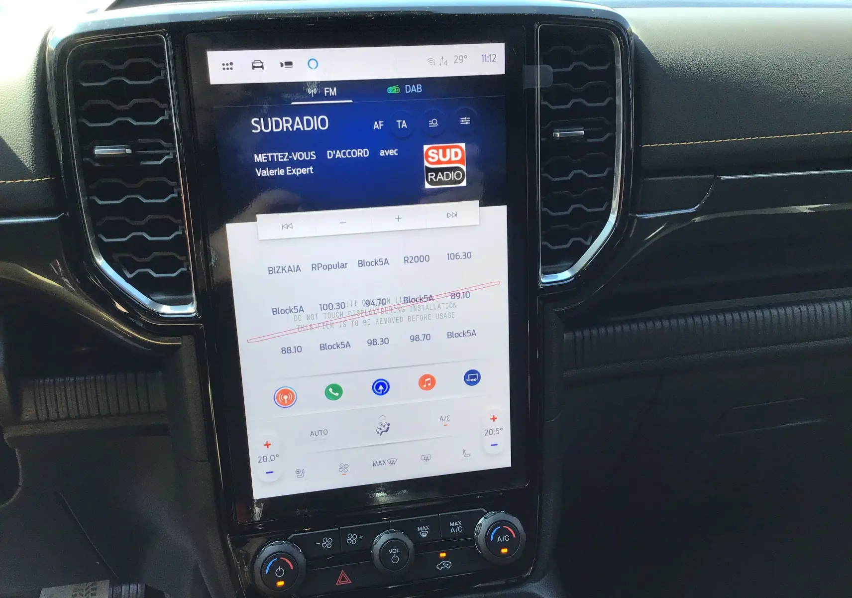 Vue rapprochée de l'écran tactile central du Ford Ranger Wildtrak 2025, affichant la radio Sud Radio et les commandes climatisation.