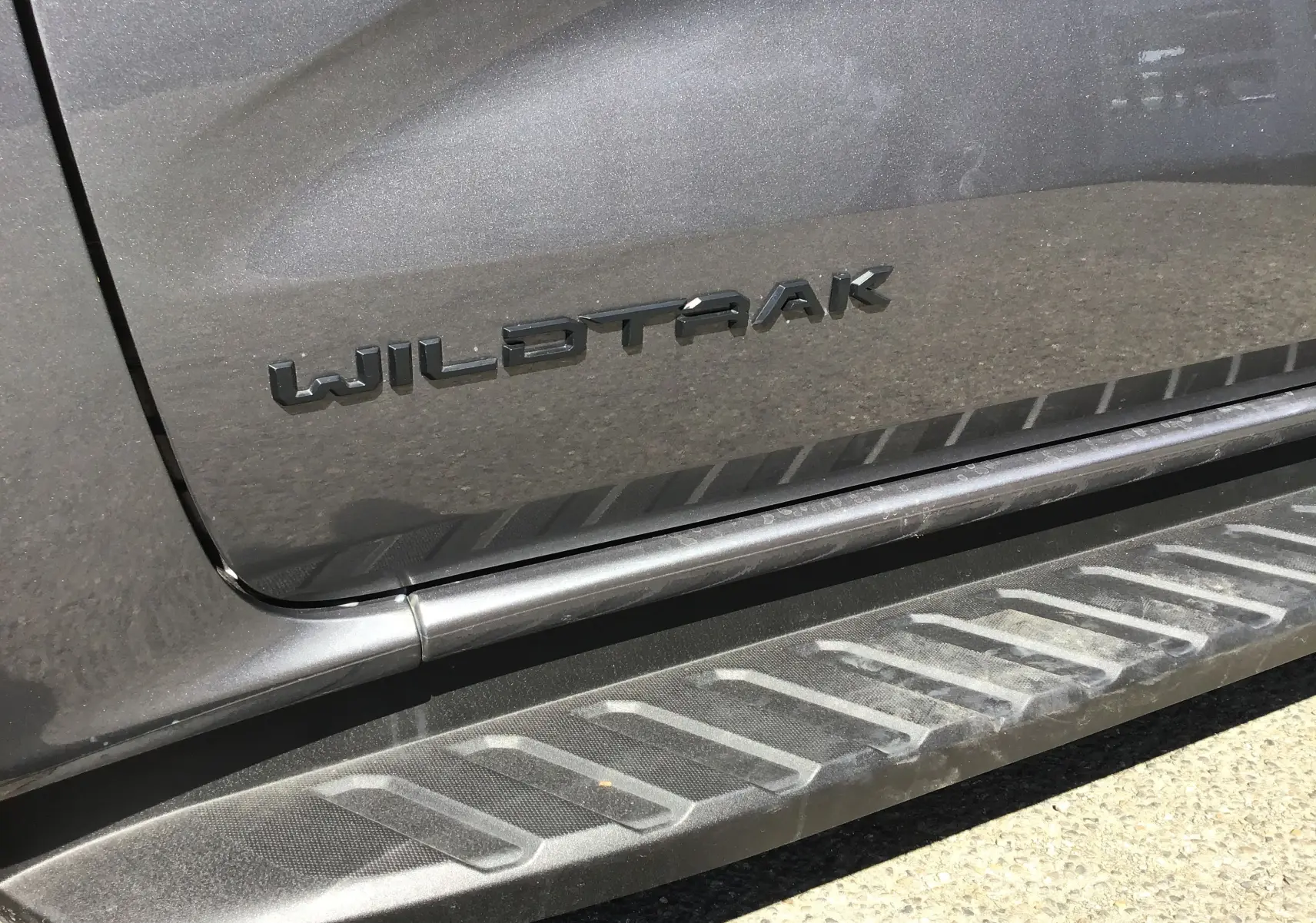 Gros plan sur l’inscription Wildtrak en relief sur la porte côté gauche d’un Ford Ranger gris carbone avec marchepied.
