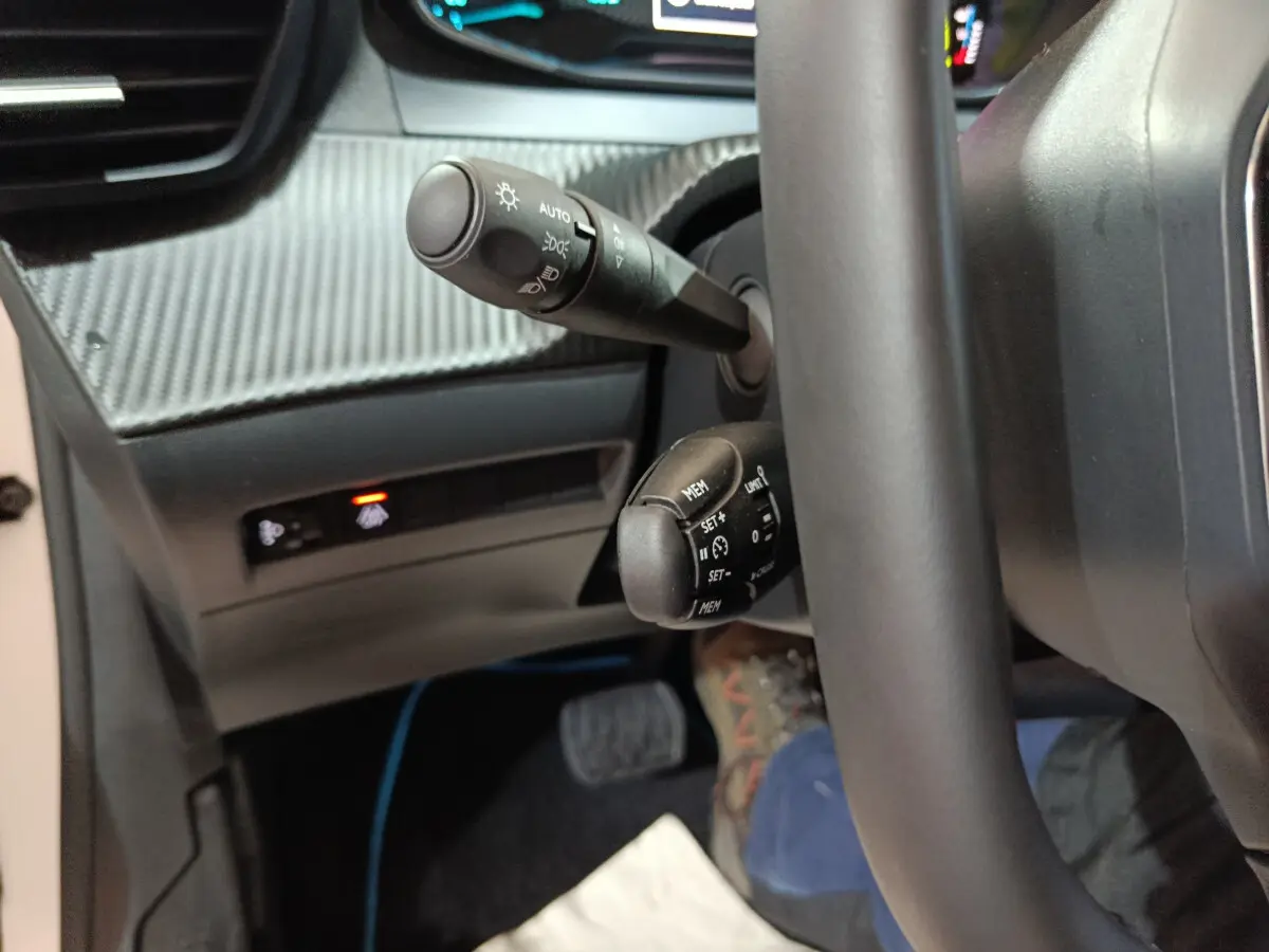 Gros plan sur les commandes au volant et tableau de bord carbone de la Peugeot 208 électrique blanche, côté conducteur.