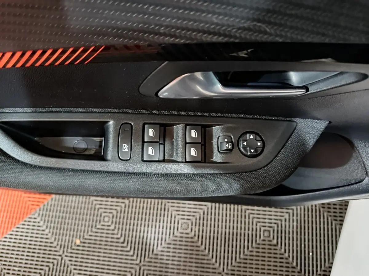 Gros plan sur la commande des vitres et rétroviseurs côté conducteur de la Peugeot 208 électrique blanche.