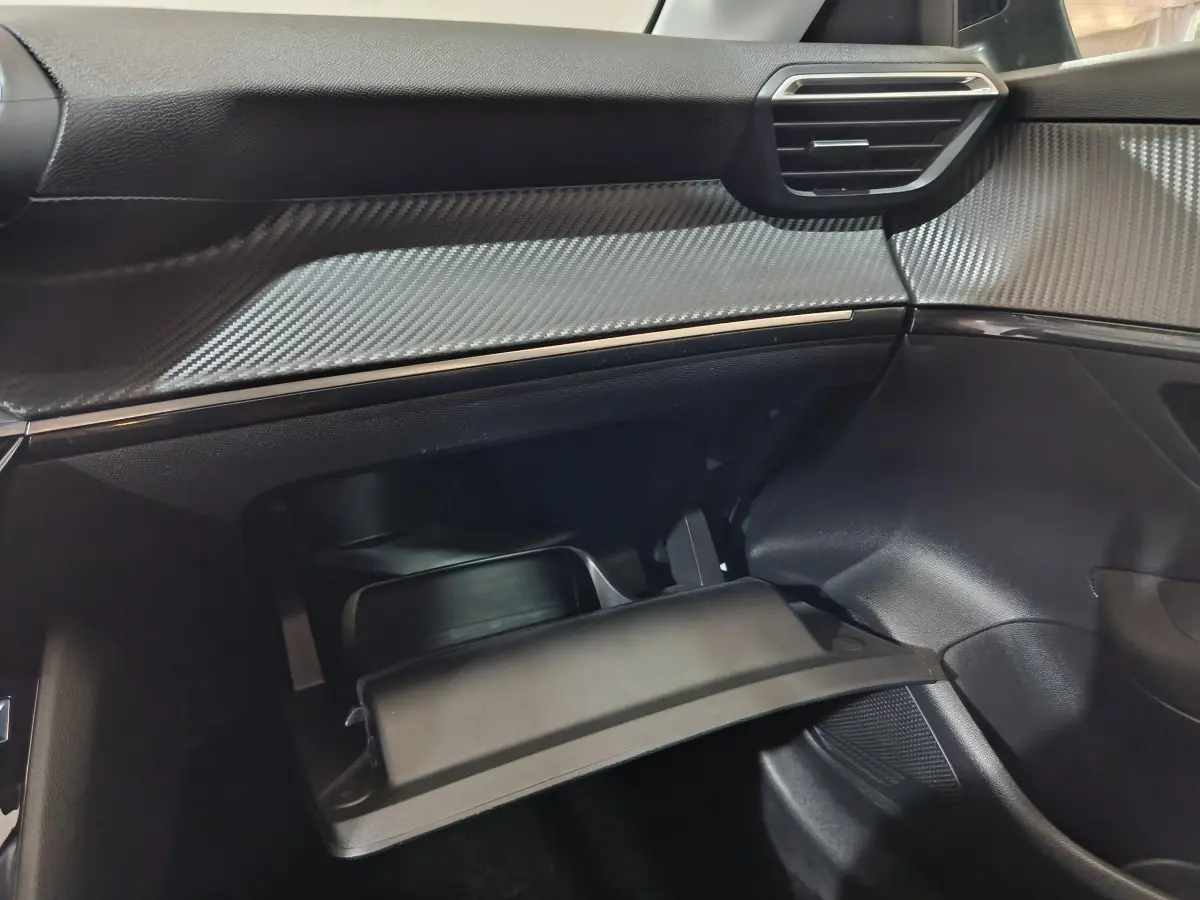 Vue intérieure côté passager de la Peugeot 208 électrique 2023, tableau de bord avec finition carbone et boîte à gants ouverte.