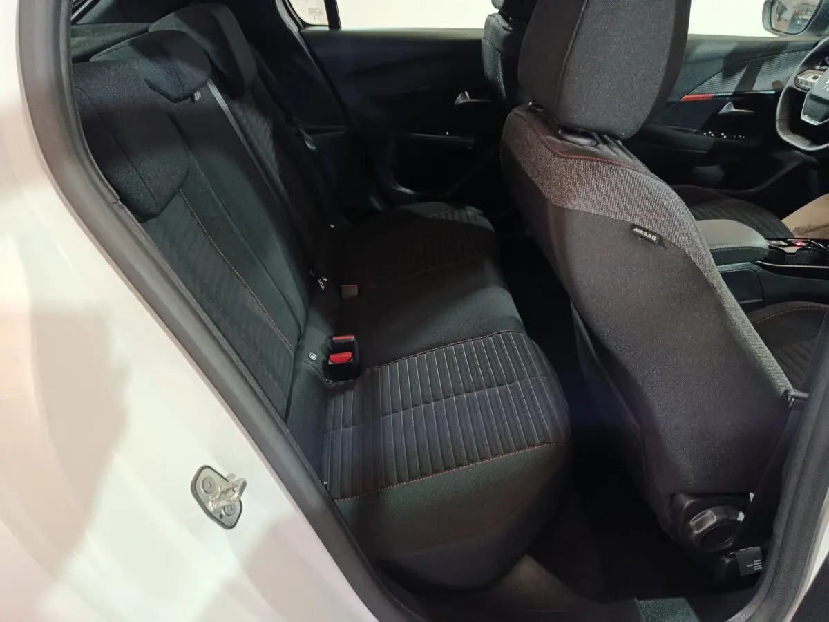 Vue intérieure côté gauche sur la banquette arrière noire avec surpiqûres rouges d'une Peugeot 208 électrique blanche 2023.