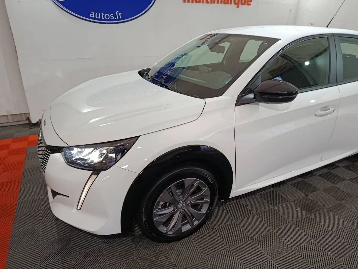 Vue 3/4 avant gauche d'une Peugeot 208 électrique blanche avec phares LED et rétroviseurs noirs brillants.