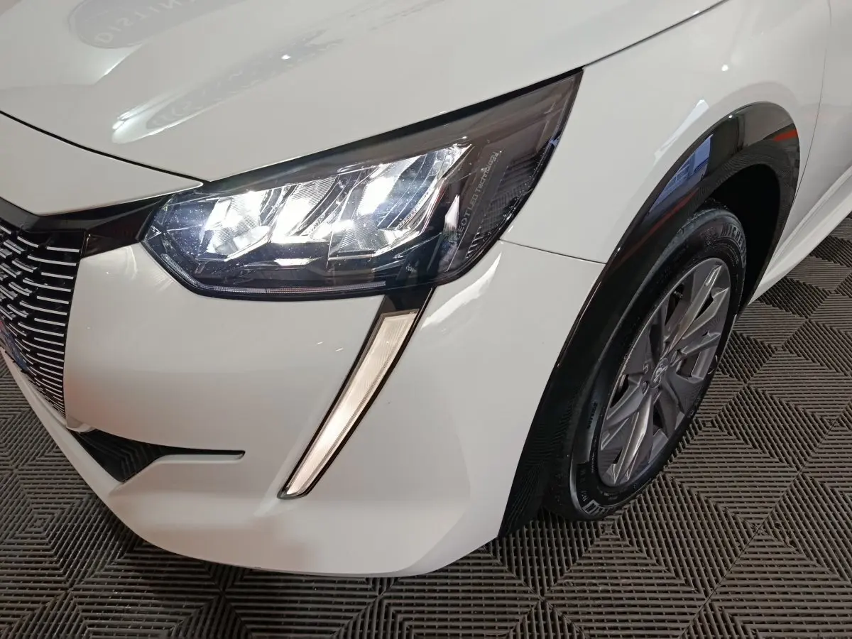 Gros plan sur l'avant droit blanc du Peugeot 208 électrique 2023, mettant en valeur le phare LED et la roue.