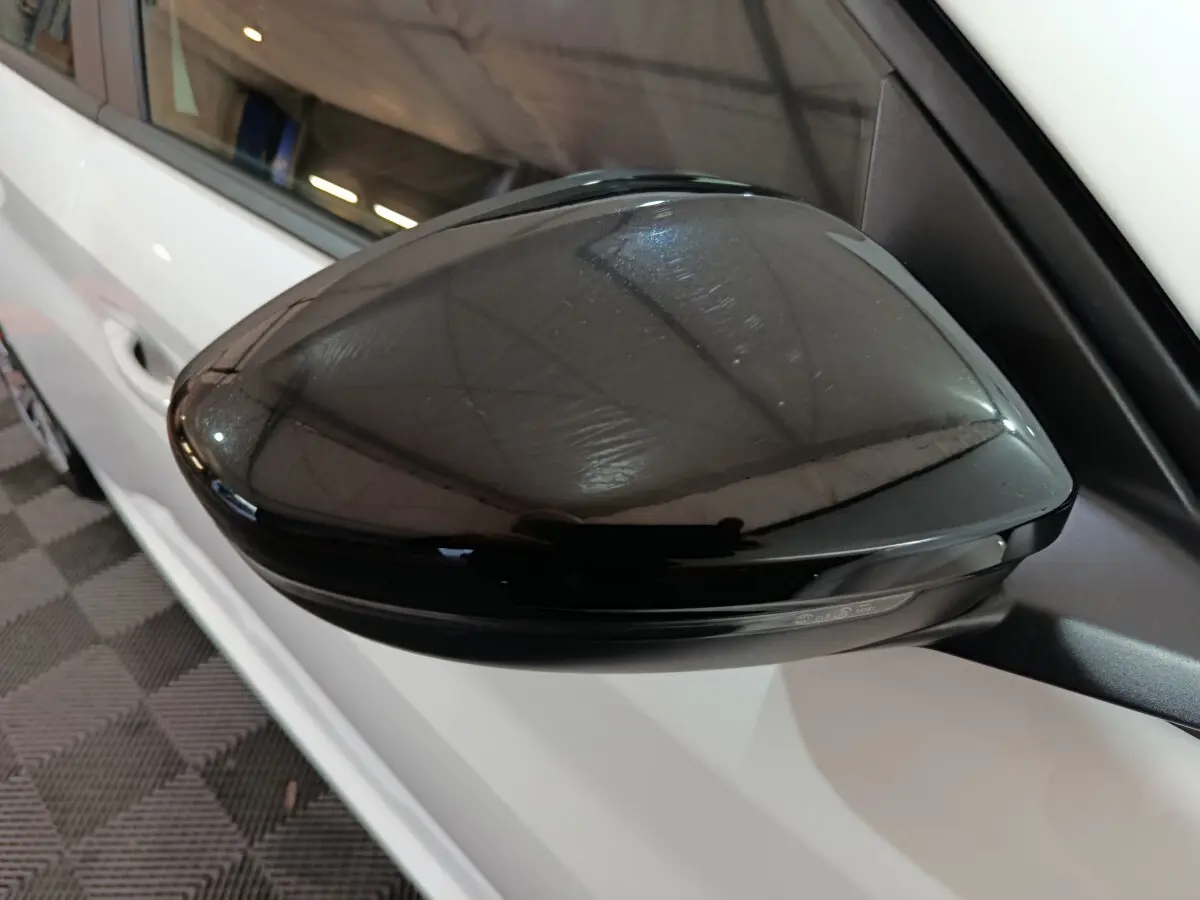 Rétroviseur noir côté gauche d'une Peugeot 208 électrique blanche vue de près en intérieur.