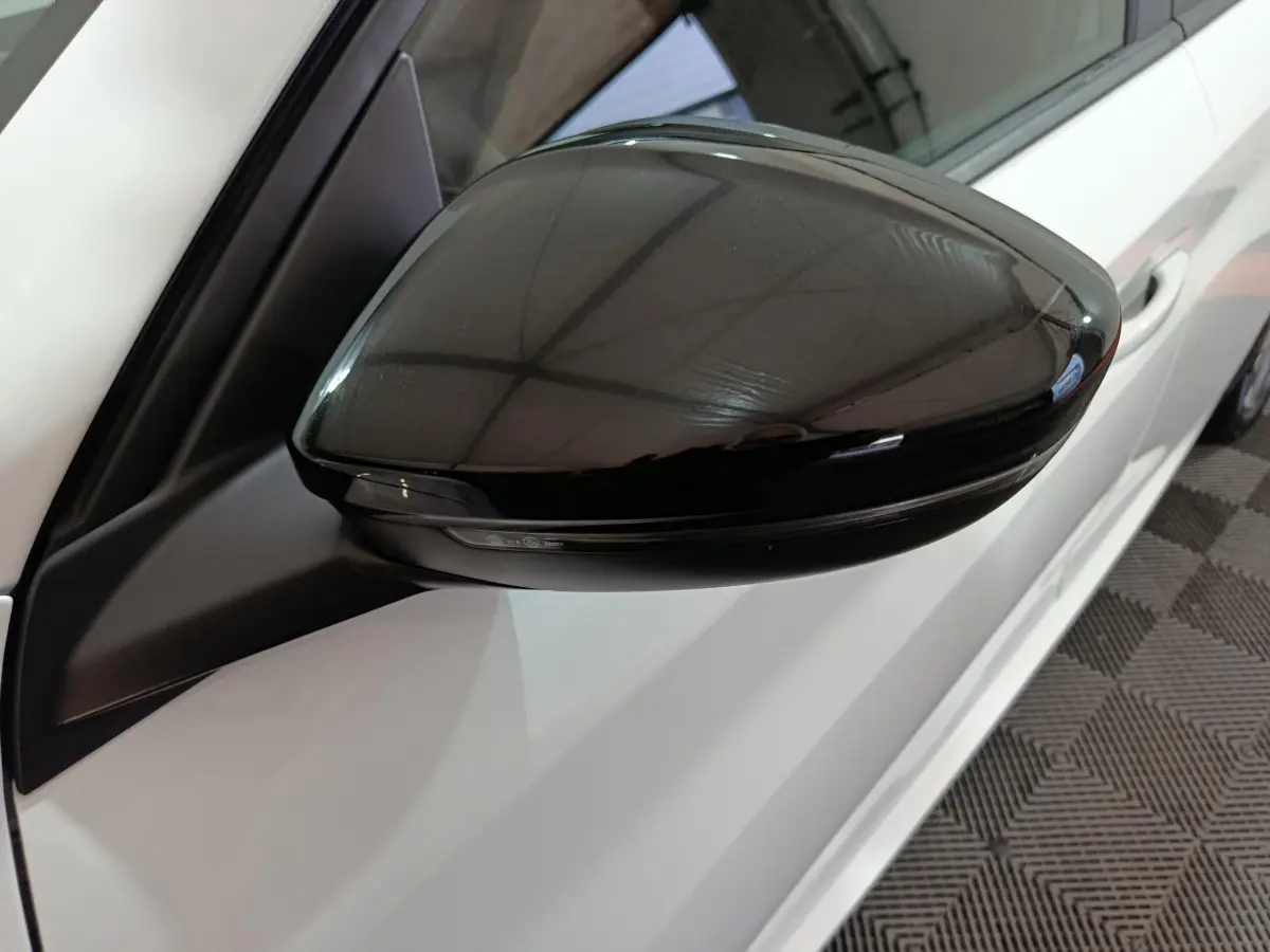 Rétroviseur noir côté gauche d'une Peugeot 208 électrique blanche vue en gros plan sur fond intérieur.