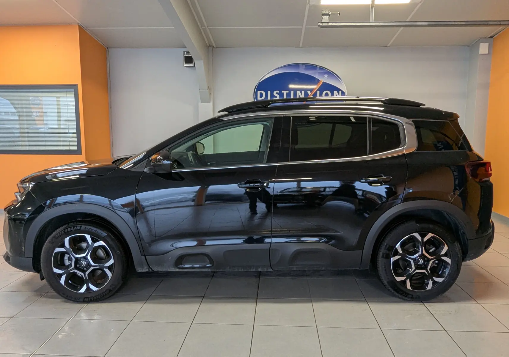 Vue de profil côté gauche d'un Citroën C5 Aircross hybride noir 2025, avec vitres arrière surteintées et barres de toit chromées.