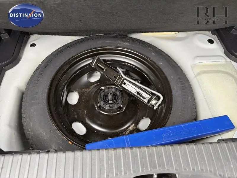 Gros plan sur la roue de secours galette noire et le cric dans le coffre d'une Citroën C3 Aircross blanche.