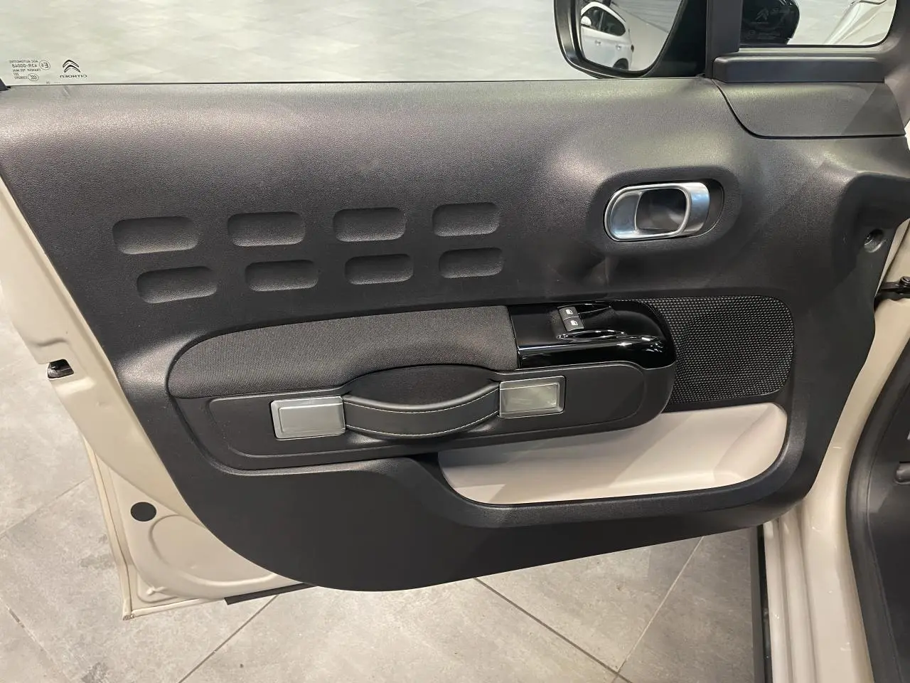 Vue rapprochée de la porte avant gauche beige clair d'une Citroën C3 2024 avec panneau noir et poignée intégrée.