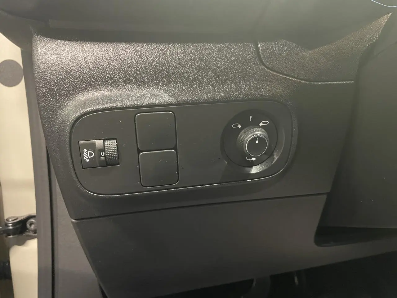 Vue rapprochée des commandes de réglage des rétroviseurs et des phares sur la porte beige clair d'une Citroën C3 2024.