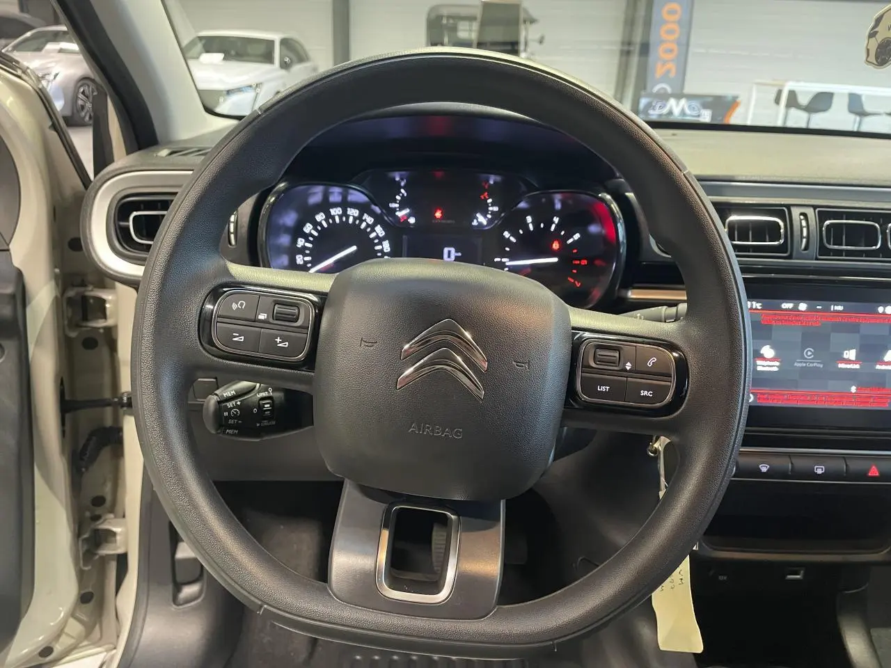 Vue intérieure centrée sur le volant noir de la Citroën C3 beige clair 2024 avec tableau de bord et écran tactile.