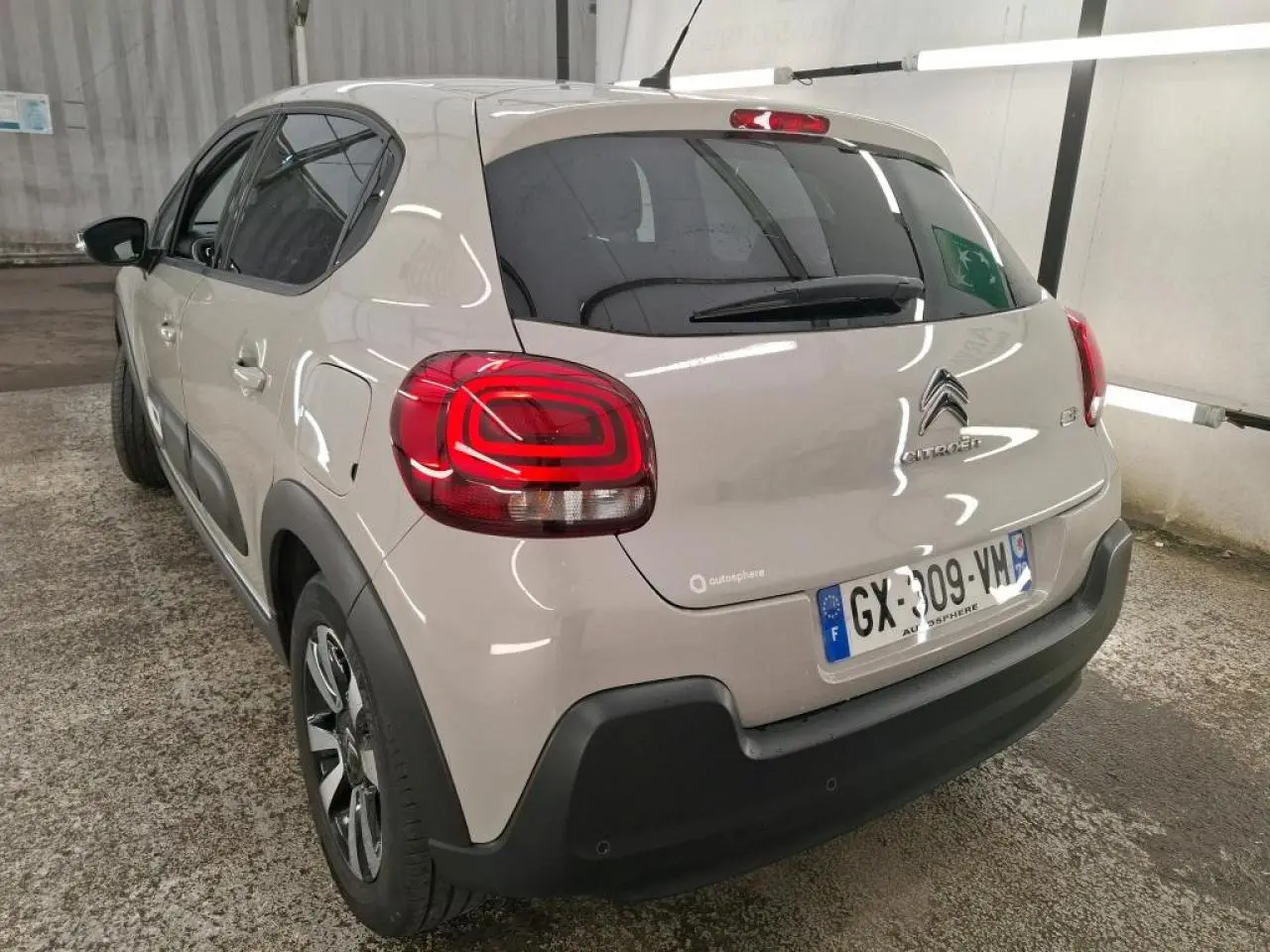 Vue 3/4 arrière gauche d'une Citroën C3 beige clair avec feux arrière LED et protections noires sur les bas de caisse.