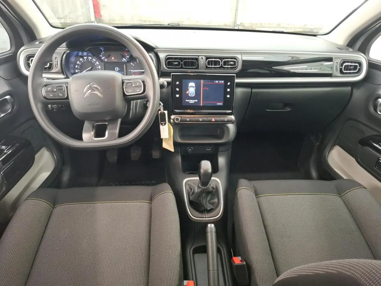 Intérieur avant du Citroën C3 2024, vue du conducteur, tableau de bord noir brillant et sièges tissu gris avec surpiqûres jaunes.