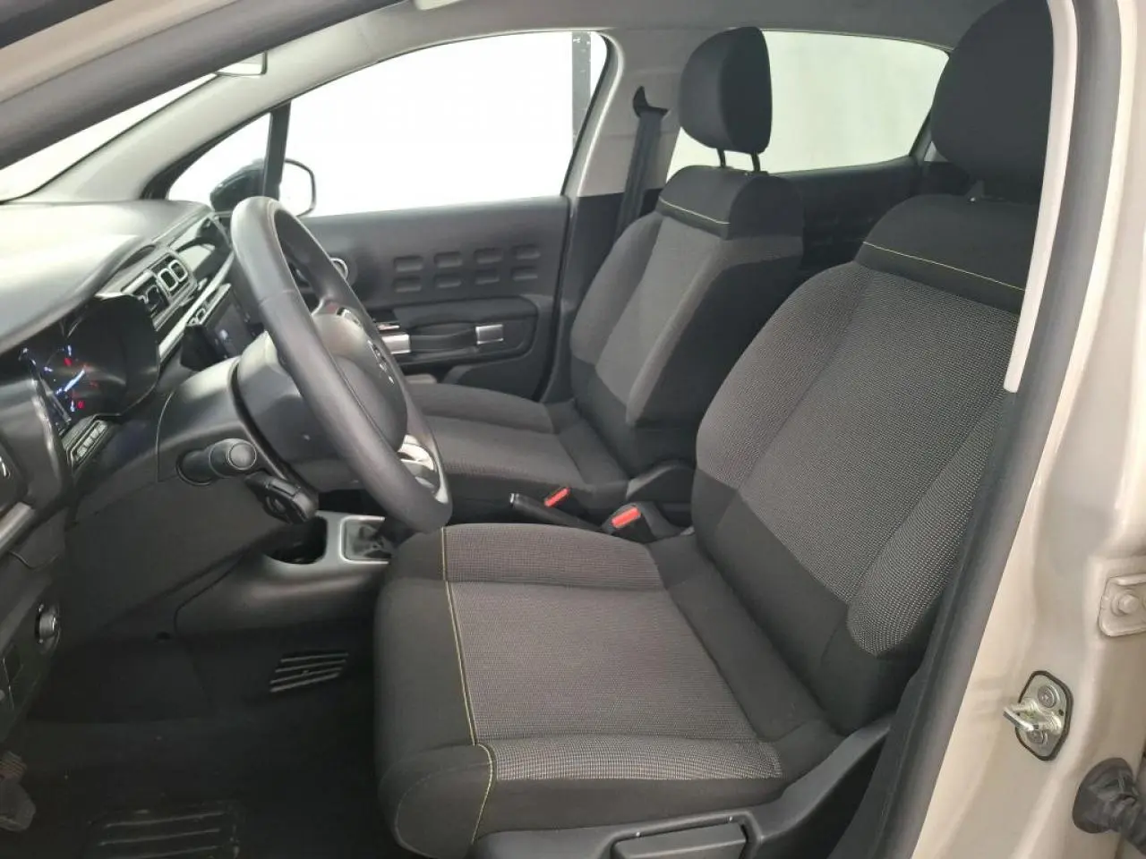 Vue intérieure côté conducteur de la Citroën C3 beige clair 2024, sièges tissu gris avec surpiqûres jaunes.