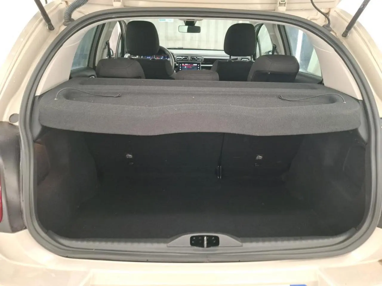 Vue arrière ouverte du coffre d'une Citroën C3 beige clair 2024, avec banquette arrière et tablette cache-bagages visibles.
